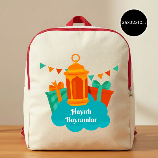 25×32×10 cm ölçülerinde doğal ham bez sırt çantası, kırmızı fermuar ve askılarla; ön yüzünde turuncu fener, renkli hediye paketleri ve üçgen bayraklı süslemelerle birlikte mavi bulut zeminde “Hayırlı Bayramlar” yazısı, sade açık renkli arka plan ve ahşap yüzey.