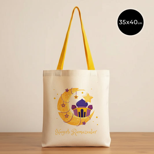 35×40 cm ölçülerinde doğal ham bez tote çanta üzerinde sarı askılar, mor fener, sarı hilal ve yıldızlardan oluşan bayram illüstrasyonu ile altında “Hayırlı Ramazanlar” yazısı; sade açık renkli arka plan ve ahşap yüzey.