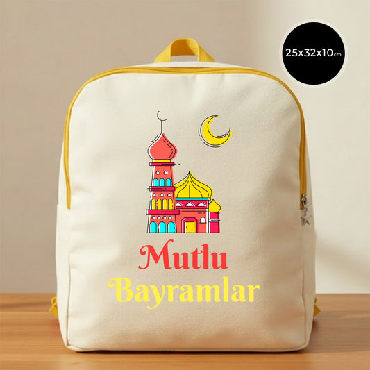 25×32×10 cm ölçülerinde doğal ham bez sırt çantası, sarı fermuar ve askılarla; ön yüzünde kırmızı–sarı tonlarında cami illüstrasyonu, sarı hilal ve altında “Mutlu Bayramlar” yazısı, sade açık renkli arka plan ve ahşap yüzey.