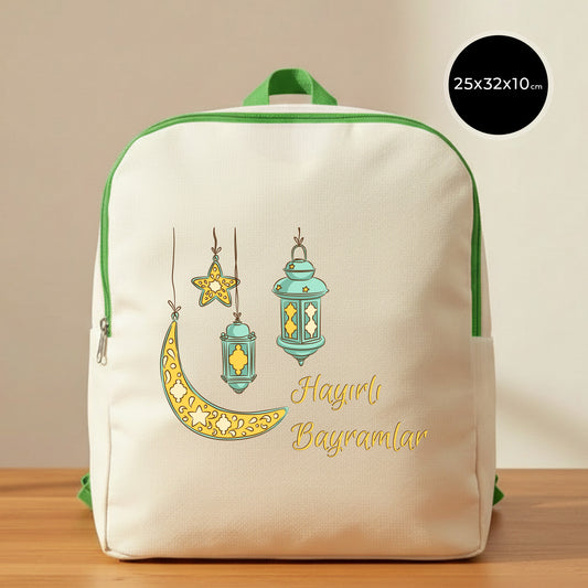 25×32×10 cm ölçülerinde doğal ham bez sırt çantası, yeşil fermuar ve askılarla; ön yüzünde asılı turkuaz fenerler, süslemeli sarı hilal ve yıldız illüstrasyonu ile sağ altta “Hayırlı Bayramlar” yazısı, sade açık renkli arka plan ve ahşap yüzey.