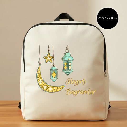 25×32×10 cm ölçülerinde doğal ham bez sırt çantası, siyah fermuar ve askılarla; ön yüzünde asılı turkuaz fenerler, süslemeli sarı hilal ve yıldız illüstrasyonu ile sağ altta “Hayırlı Bayramlar” yazısı, sade açık renkli arka plan ve ahşap yüzey.