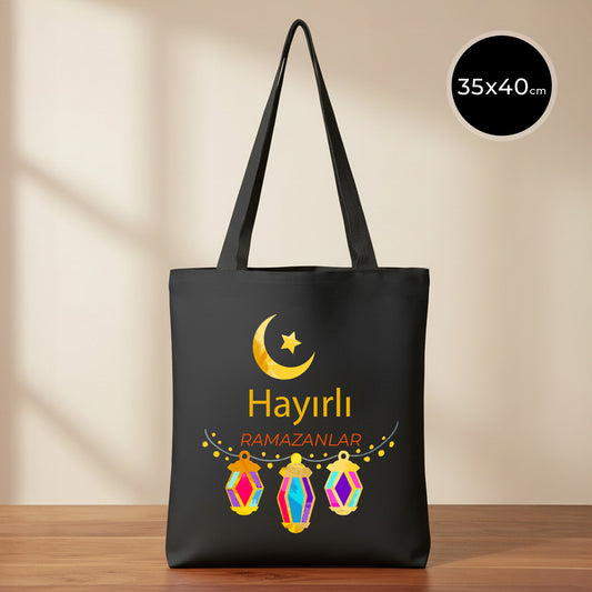 35×40 cm ölçülerinde siyah ham bez tote çanta üzerinde üstte sarı hilal ve yıldız, altta üç adet renkli asılı fener illüstrasyonu ve ortada “Hayırlı Ramazanlar” yazısı; siyah omuz askıları ve sade açık renkli arka plan.