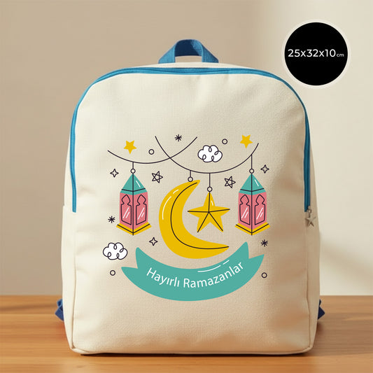 25×32×10 cm ölçülerinde doğal ham bez sırt çantası, turkuaz fermuar ve askılarla; ön yüzünde asılı pembe–turkuaz fenerler, sarı hilal ve yıldız illüstrasyonu ile turkuaz şerit içinde “Hayırlı Ramazanlar” yazısı, sade açık renkli arka plan ve ahşap yüzey.