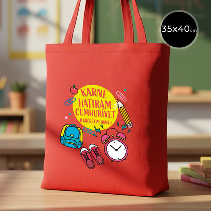 Renkli ve sıcak bir sınıf ortamında, ahşap masada sergilenen canlı kırmızı 35x40 cm gabardin bez çanta, 70 cm saplı.