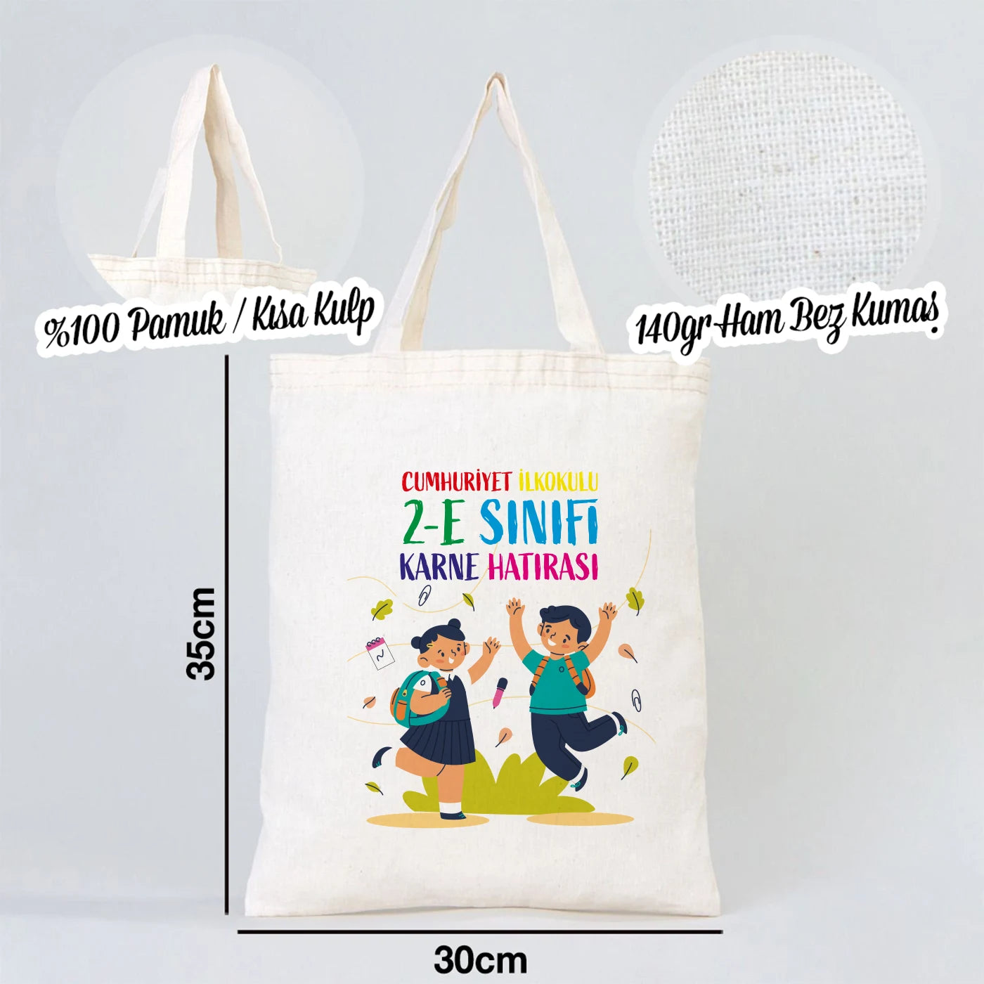 Rengarenk ve sıcak bir sınıf ortamında, ahşap masada sergilenen 30x35 cm kısa kulplu ham pamuk bez çanta.