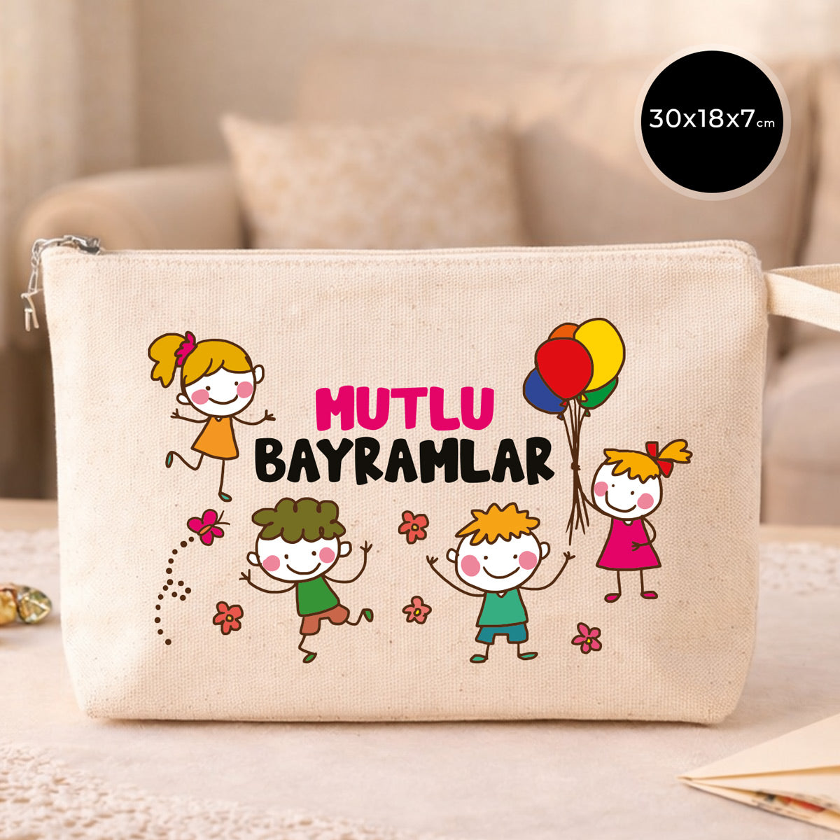 30×18×7 cm ölçülerinde doğal ham bez fermuarlı çanta üzerinde çocuk figürleri, balonlar ve çiçeklerle birlikte “Mutlu Bayramlar” yazısı; arka planda açık renkli kanepe.