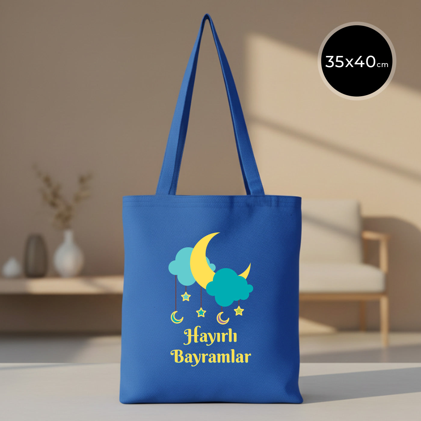 35x40 cm mavi gabardin bez tote çanta; ön yüzde sarı hilal, turkuaz bulutlar, sarkan yıldız-ay figürleri ve “Hayırlı Bayramlar” yazısı baskısı.