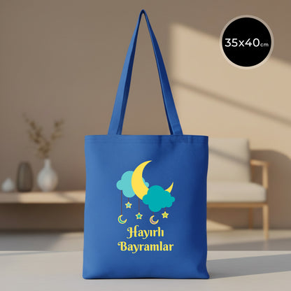 35x40 cm mavi gabardin bez tote çanta; ön yüzde sarı hilal, turkuaz bulutlar, sarkan yıldız-ay figürleri ve “Hayırlı Bayramlar” yazısı baskısı.