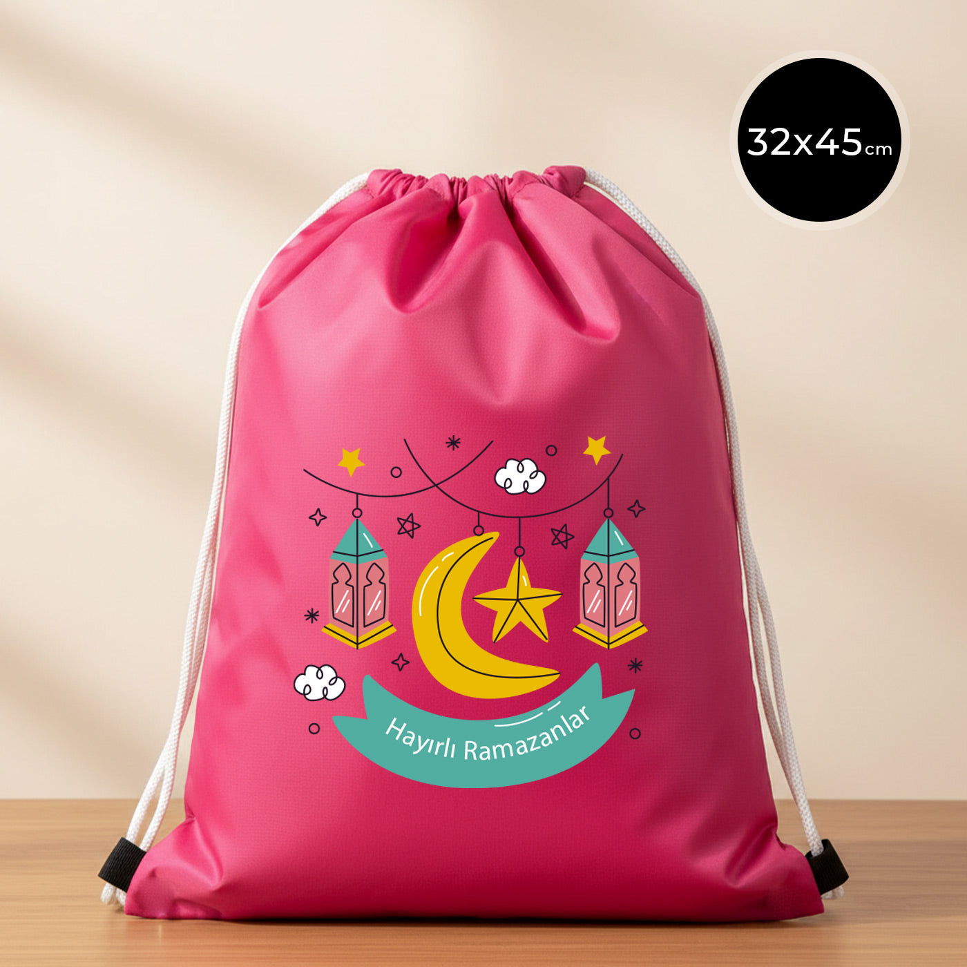 32×45 cm ölçülerinde fuşya imperteks ip büzgülü sırt çantası üzerinde asılı pembe–turkuaz fenerler, sarı hilal ve yıldız illüstrasyonu ile turkuaz şerit içinde “Hayırlı Ramazanlar” yazısı; beyaz ip askılar ve sade açık renkli arka plan.