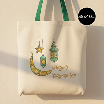 35×40 cm ölçülerinde doğal ham bez tote çanta üzerinde asılı turkuaz fenerler, sarı yıldız ve süslemeli hilal illüstrasyonu ile altında “Hayırlı Bayramlar” yazısı; yeşil askılı, açık renkli arka plan.